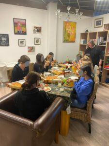 Flere personer sitter rundt bord med mat og gjenstander