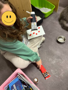 Person sitter på gulvet med papp, saks og små gjenstander rundt seg