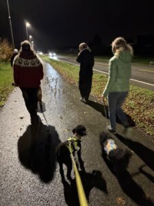 Personer går utendørs med hund i bånd i mørket